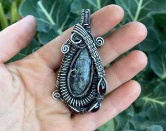 May include: A silver wire wrapped pendant featuring a grey and black gemstone with two red gemstones on the bottom.