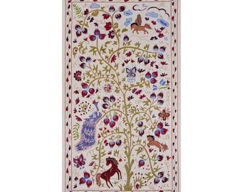 May include: Rectangular textile with a cream background, featuring a central tree design with red, blue, and purple flowers, a peacock, and horses. The border is a red and cream pattern. The artwork is likely hand-stitched.