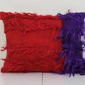 Könnte beinhalten: Rotes und violettes Dekokissen mit einer zotteligen Textur. Das Kissen ist aus einem weichen, flauschigen Material gefertigt und hat einen einzigartigen, handgefertigten Look.