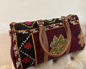 Puede incluir: Una bolsa de viaje de lona con estampado burdeos, negro y verde con asas de cuero marrón.