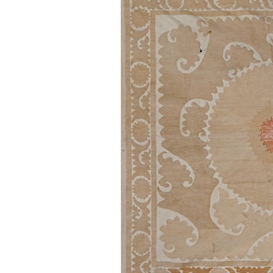 May include: A section of a beige and cream-colored rug with an intricate floral design. The rug features a central medallion and a border with repeating patterns. The design includes cream-colored floral motifs and a red accent in the center.