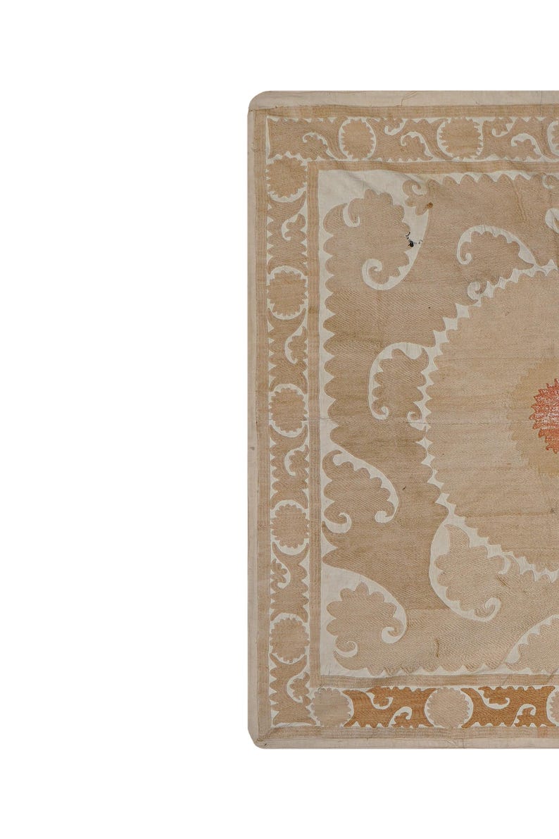 May include: A section of a beige and cream-colored rug with an intricate floral design. The rug features a central medallion and a border with repeating patterns. The design includes cream-colored floral motifs and a red accent in the center.