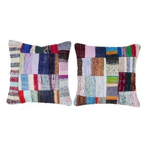 May include: Two square throw pillows with a patchwork design. Each pillow features a variety of colorful fabric squares in shades of red, blue, green, and cream. The pillows are placed against a white background.