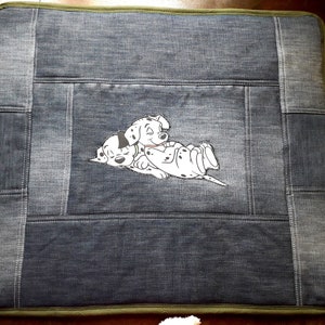 May include: A denim dog bed with a green border and an embroidered image of two dalmatian puppies sleeping.