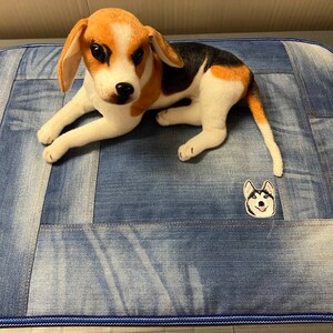 以下が含まれることがあります： 青いデニムの犬用ベッドの上に、白黒の犬のぬいぐるみが置かれています。ベッドは青い縁取りがあり、ハスキー犬の小さな刺繍が施されています。