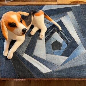 Puede incluir: Un perro de peluche marrón y blanco acostado sobre una alfombra de patchwork de mezclilla con un borde de cuero marrón.