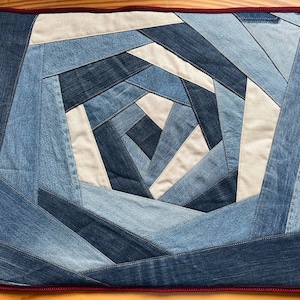 May include: A blue and white denim quilt with a spiral pattern. The quilt is edged with a red trim.