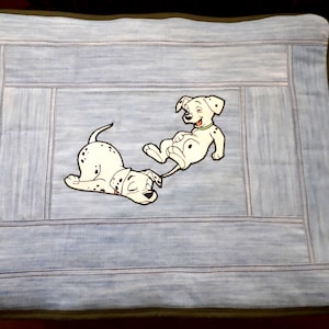 Puede incluir: Una almohada de mezclilla azul con dos cachorros dálmatas bordados. Un cachorro está acostado y el otro está sentado con la lengua afuera.