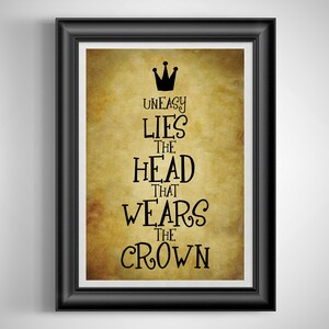 May include: Framed art print with the quote "Uneasy Lies the Head That Wears the Crown" in black lettering. The background has a vintage, parchment-like appearance. The black frame adds a classic touch to the artwork.
