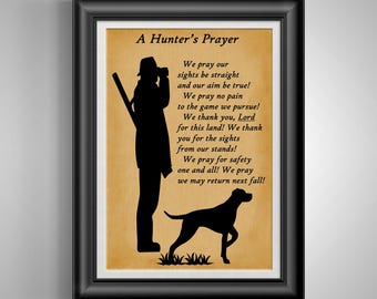 May include: Framed print featuring a silhouette of a hunter with a rifle and a dog, set against a tan background. The text "A Hunter's Prayer" and a prayer are printed on the image. The frame is black.