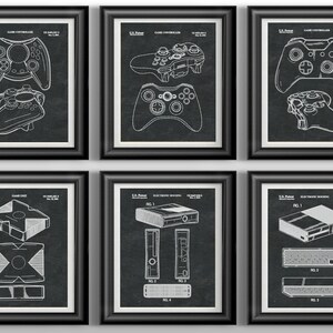 May include: A set of six black framed prints featuring vintage patent drawings of various video game controllers and consoles. The prints are all in black and white and feature detailed illustrations of the products.