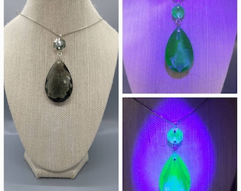 May include: A silver necklace with a teardrop-shaped pendant. The pendant is clear and has a textured surface. The pendant glows green under a black light.