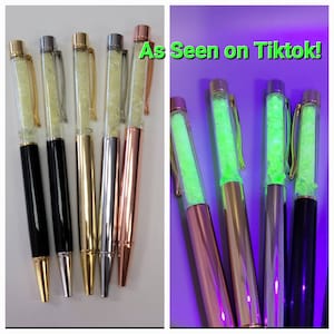 May include: Five pens with clear barrels filled with glitter. The pens are black, gold, silver, and rose gold. The glitter glows green under a black light. "As Seen on Tiktok!" is written in green text on a purple background.