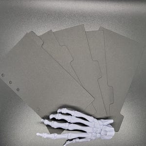 May include: Six gray paper dividers with rounded corners and holes for a disc bound planner.