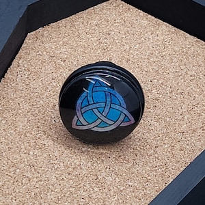 May include: A black and blue circular plug with a Celtic knot design. The knot is a triquetra, a symbol of the trinity.