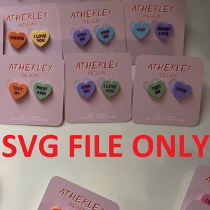 May include: A set of 10 colorful heart-shaped candy conversation pieces with various messages, including "Kiss Me", "I Love You", "Text Me", "First Kiss", "Sweet Love", "You", "Be Mine", "Hugs", "XOXO", and "Love". The candy pieces are displayed on small pink cards with the brand name "ATHERLEY DESIGNS" printed on them.