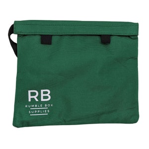 May include: A green zippered pouch with a black strap and two black tabs. The pouch has the text "RB RUMBLE BOX SUPPLIES" printed on the front.