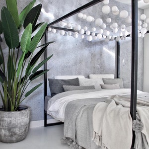 May include: A gray bed frame with a white bedspread and gray throw blanket. The bed is decorated with white cotton ball lights.