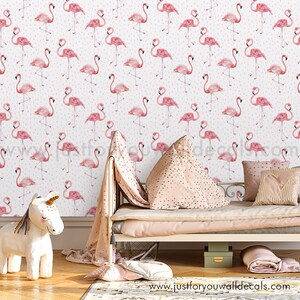 May include: Pink flamingo wallpaper with white polka dots. The wallpaper is shown in a nursery setting with a white bed, pink bedding, and a unicorn toy.