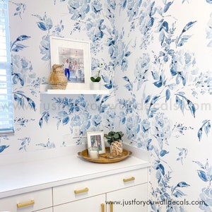 May include: A room with white cabinetry and a white countertop, adorned with a floral wallpaper featuring blue watercolor flowers. A white shelf displays a framed photo and decorative items. Gold hardware accents the cabinets.