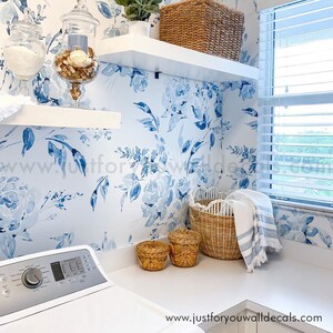 May include: A laundry room with a floral wallpaper in shades of blue and white. White shelves hold a woven basket and decorative jars. Woven baskets and a washing machine are also visible. The text "justforyouwalldecals.com" is at the bottom.