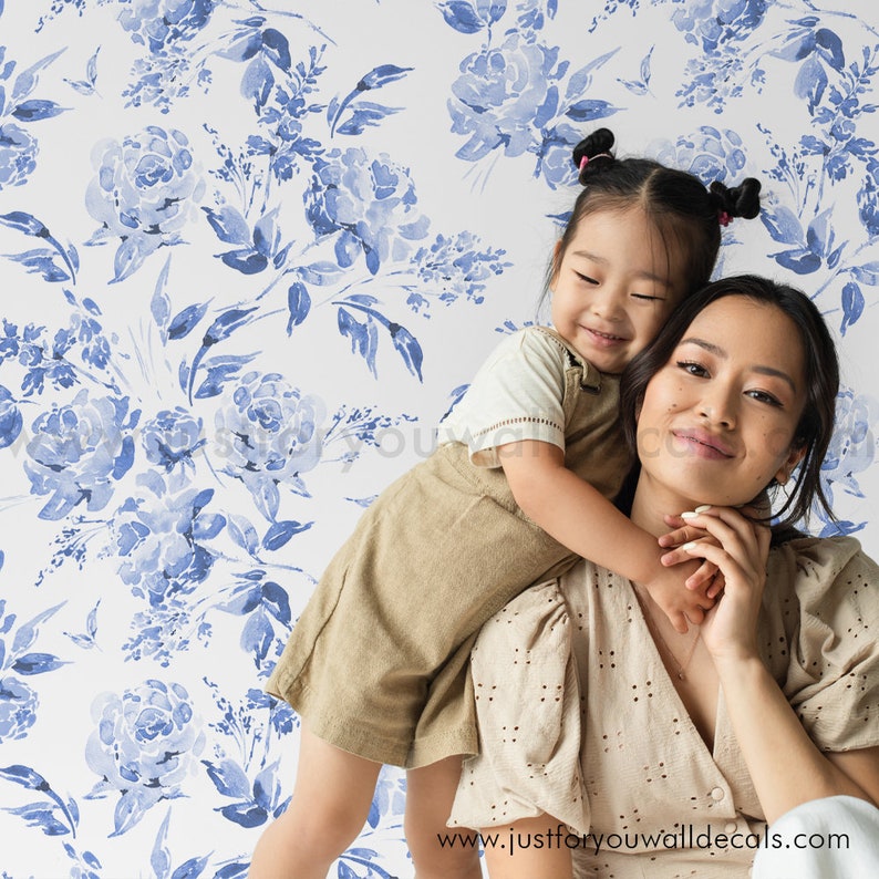 May include: A white background is covered with a blue floral pattern. A woman and a child are in front of the wallpaper. The woman is wearing a beige top, and the child is wearing a beige overall. The website address "www.justforyouwalldecals.com" is visible.