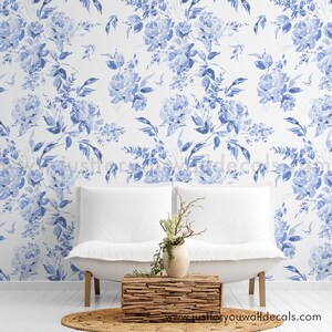 May include: A white sofa with a wooden coffee table and a vase of flowers sits in front of a wall covered in blue floral wallpaper. The wallpaper features watercolor-style blue roses and leaves on a white background. A round, woven rug is on the floor.