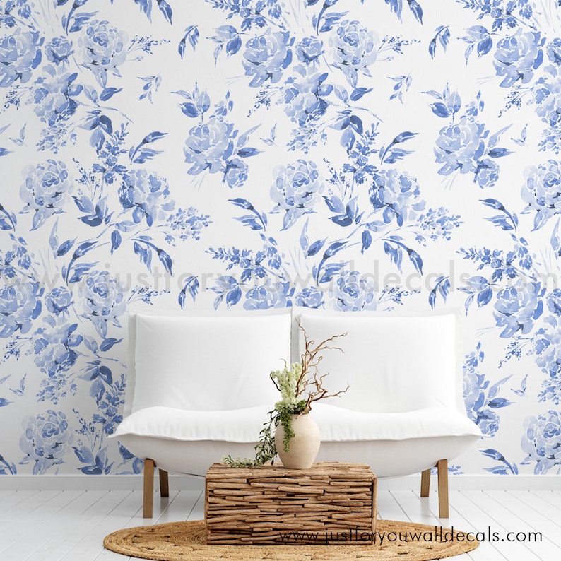 May include: A white sofa with a wooden coffee table and a vase of flowers sits in front of a wall covered in blue floral wallpaper. The wallpaper features watercolor-style blue roses and leaves on a white background. A round, woven rug is on the floor.