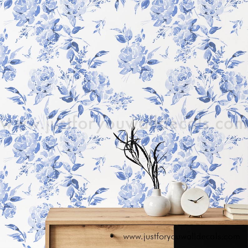 May include: Watercolor floral wallpaper in shades of blue and white. The design features large, blooming roses and other floral elements. A wooden cabinet with white vases, a clock, and books is in the foreground. The website address "www.justforyouwalldecals.com" is visible.