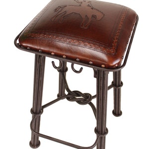 May include: A brown leather bar stool with a tooled design of a cowboy riding a horse. The stool has a metal frame with a knotted base.