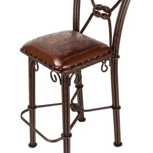 May include: A brown metal bar stool with a square, embossed leather seat. The back of the stool features a decorative knot design. The stool has a footrest and measures approximately 42 inches high.