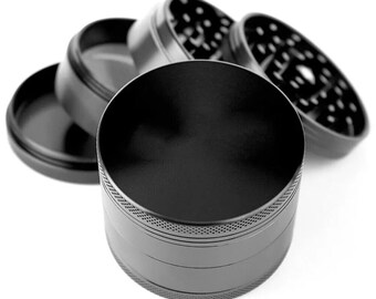 May include: A black, four-piece herb grinder with a cylindrical design. The grinder is made of metal and has a matte finish. The top piece is open, revealing the grinding teeth. The other pieces are disassembled and displayed around the main body.