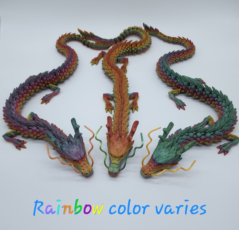 May include: Three rainbow-coloured dragon figurines are displayed against a white background. The text "Rainbow colour varies" is at the bottom. Each dragon has a detailed, textured design.