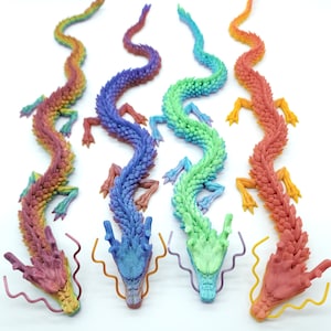 May include: Four articulated dragon figurines in rainbow hues. Each dragon features a distinct colour gradient, with shades of red, orange, yellow, green, blue, and purple. The dragons are displayed on a white surface, highlighting their intricate design.