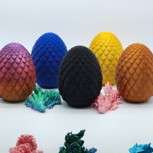 May include: Six decorative dragon eggs in various colors, including purple, blue, black, yellow, and bronze. Small dragon figurines in multiple colors are scattered around the eggs. The eggs have a textured, scaled appearance.