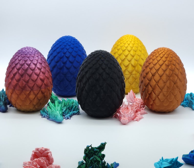 May include: Six decorative dragon eggs in various colors, including purple, blue, black, yellow, and bronze. Small dragon figurines in multiple colors are scattered around the eggs. The eggs have a textured, scaled appearance.
