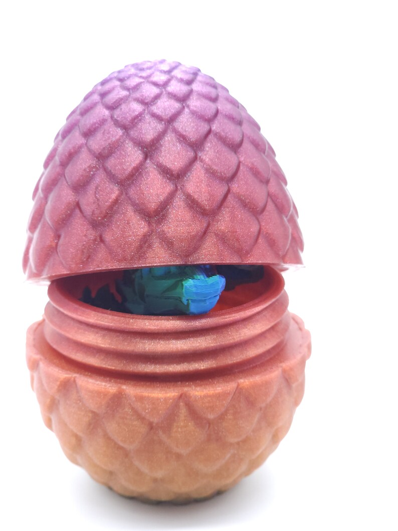 May include: A decorative dragon egg, split open to reveal a colorful interior. The egg is a gradient of pink and orange, with a textured, scale-like pattern. The interior shows blue and green colors.