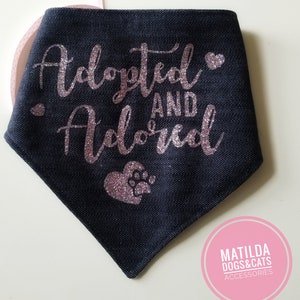 May include: A black denim dog bandana with pink glitter lettering that says "Adopted and Adored" with a pink glitter heart and paw print.
