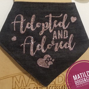 May include: Black denim bandana with pink glitter lettering that reads "Adopted and Adored" with a pink glitter heart and paw print.