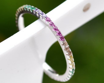 Puede incluir: Un fino anillo de banda de plata con un arcoíris de pequeñas piedras preciosas engastadas en la banda.