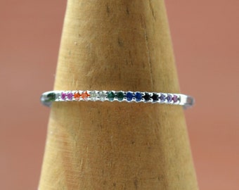 Puede incluir: Un anillo de banda de plata con una banda delgada engastada con pequeñas piedras preciosas de arcoíris.