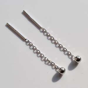 May include: A pair of silver dangle earrings with small round balls at the end of each chain.