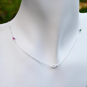 May include: A silver chain necklace with three small gemstones: a pink, a purple, and a green stone.