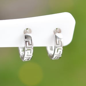 May include: A pair of silver hoop earrings with a Greek key design.