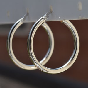 May include: A pair of silver hoop earrings hanging from a display stand. The earrings are simple and classic, with a smooth, polished finish.