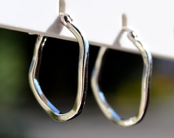 May include: A pair of silver hoop earrings with an irregular, slightly rounded, geometric shape.