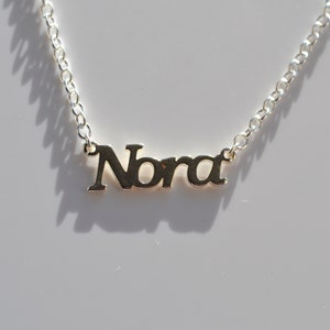 May include: Silver necklace with the name "Nora" spelled out in cursive.