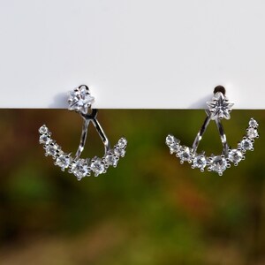May include: A pair of silver earrings featuring a crescent moon design with a star at the top. The earrings are embellished with clear cubic zirconia stones.