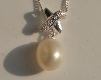 May include: A silver necklace with a pearl pendant and a silver charm in the shape of a cross. The charm is decorated with small clear stones.