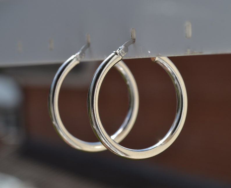 May include: A pair of silver hoop earrings hanging from a display stand. The earrings are simple and classic, with a smooth, polished finish.